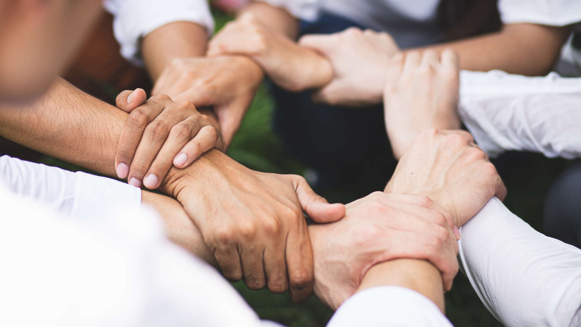 Nahaufnahme von mehreren übereinanderliegenden Händen, die sich gegenseitig halten als Symbol für Demokratie